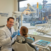 A friendly male dentist in a clean, modern clinic on Broadway in Vancouver, providing hygienic care to a female patient.