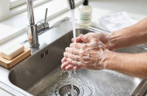 A close-up of hands being washed thoroughly with soap under running water, visible lather, clean sink area, bright lighting, emphasis on hygiene and cleanliness.